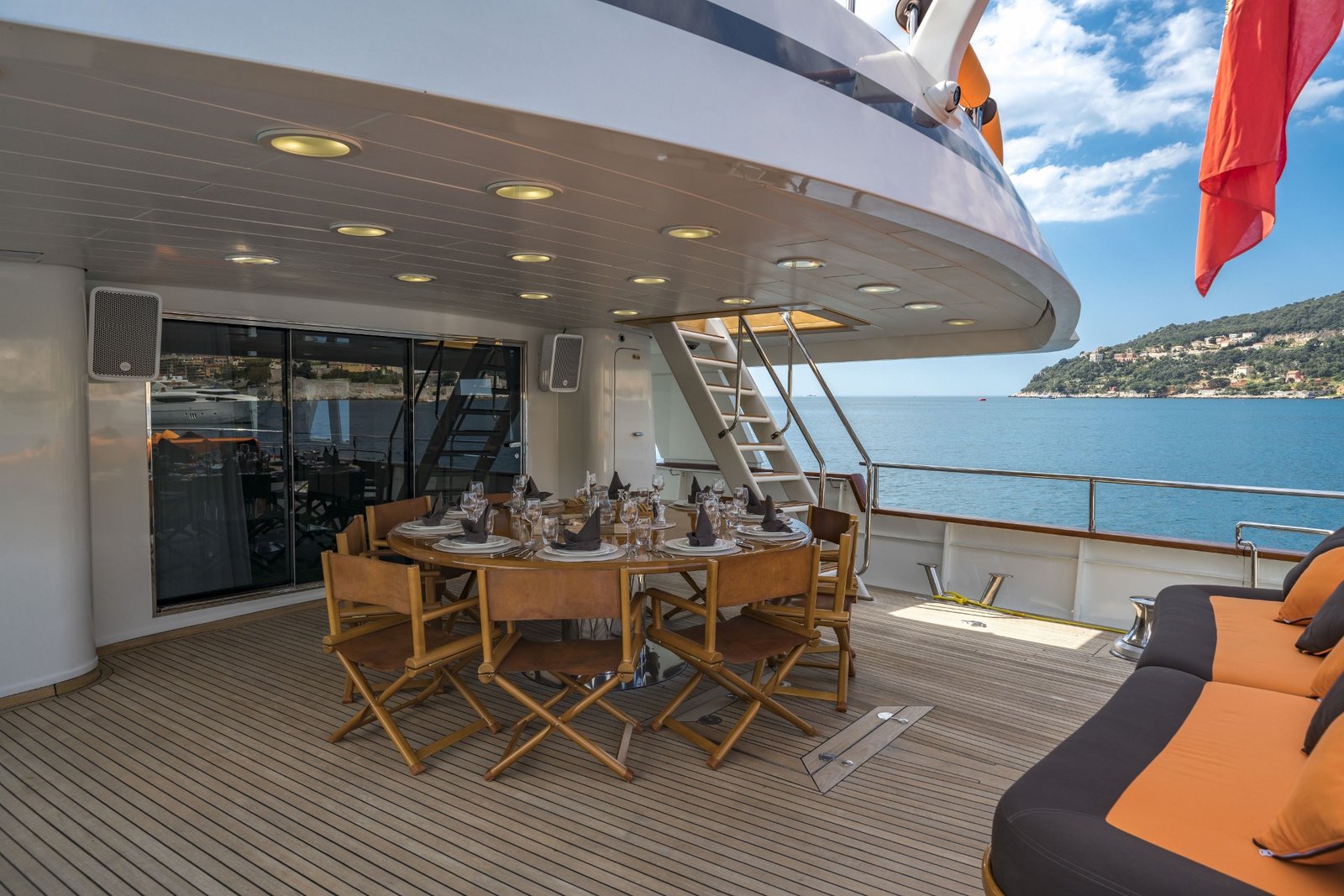 Aft deck alfresco dining — table set for eight, Red Ensign flying, Côte d'Azur beyond